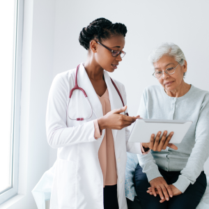 Image of a doctor with black skin and a long, white labcoat and black glasses reviewing a chart with a patient.